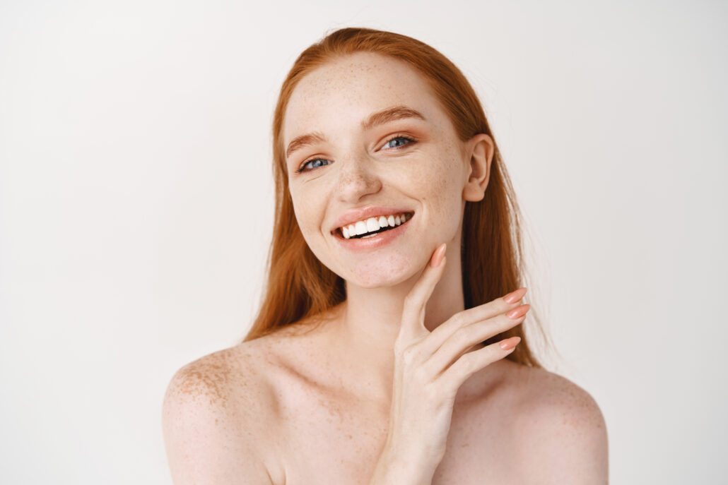 Donna sorridente che si tocca il viso, pelle luminosa e curata dopo la routine skincare